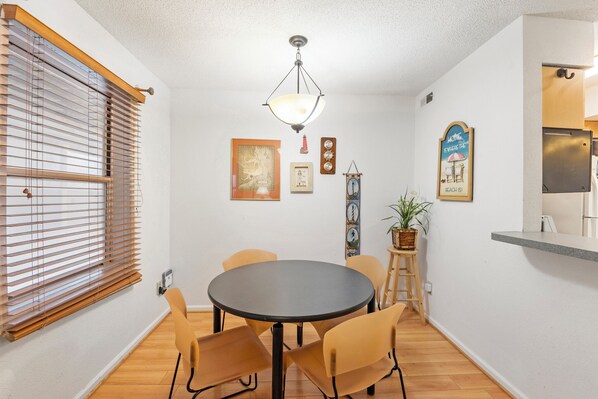 A dining area with a round table, four chairs, a hanging light fixture, and wall-mounted decorations. - Charming Condo in Kill Devil Hills (Kill Devil Hills)