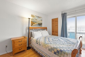 A bedroom with a bed, a bedside table, a lamp, a painting on the wall, and a view through a window.