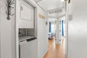 A narrow hallway with a white wall, a door leading to a bedroom, and a small kitchenette area with a stove and sink. - Charming Condo in Kill Devil Hills (Kill Devil Hills)