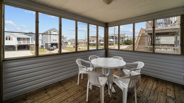 A covered patio with a wooden floor and white plastic chairs around a white table.