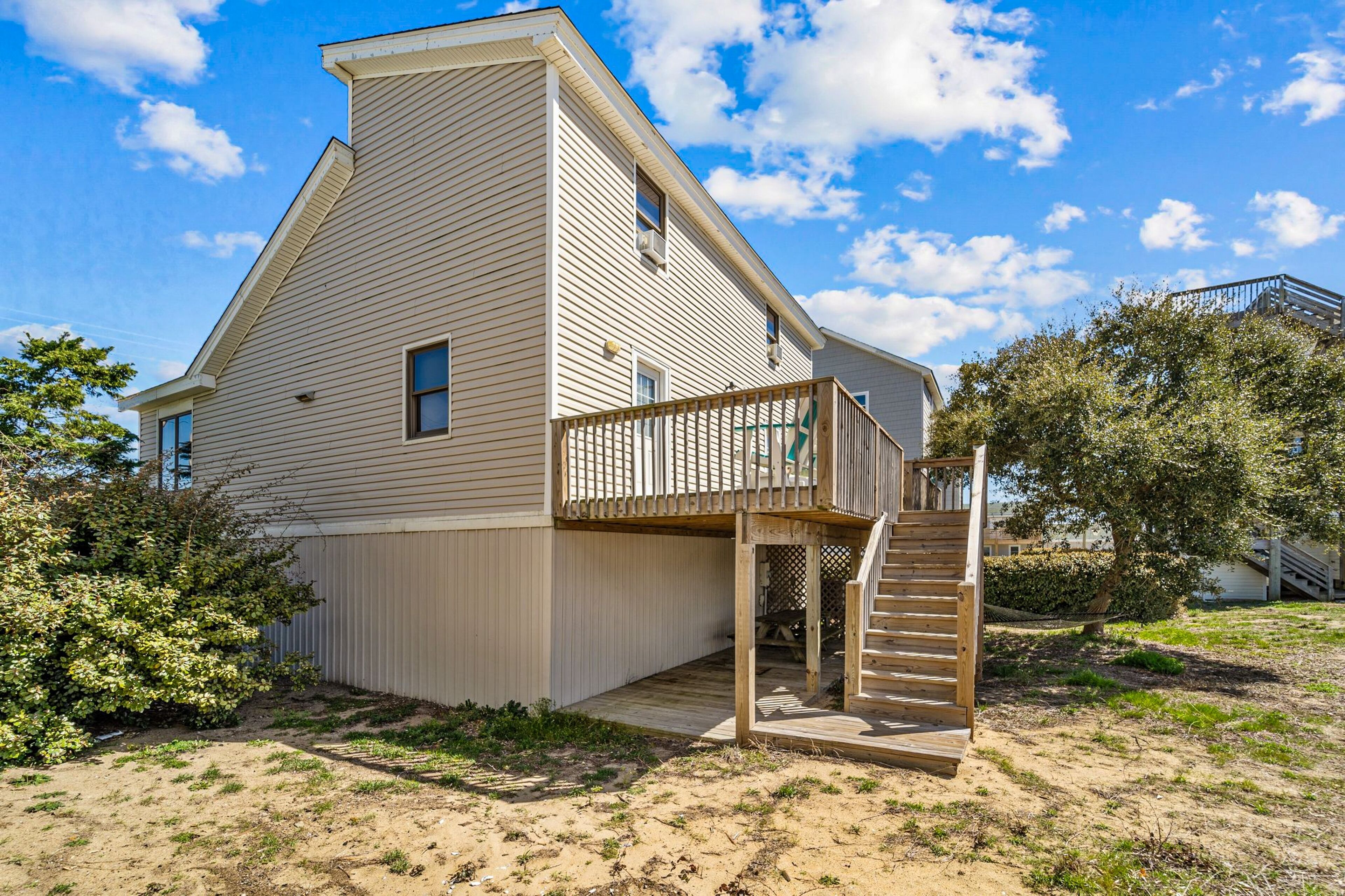 A two-story house with a wooden deck and a staircase leading to a balcony.