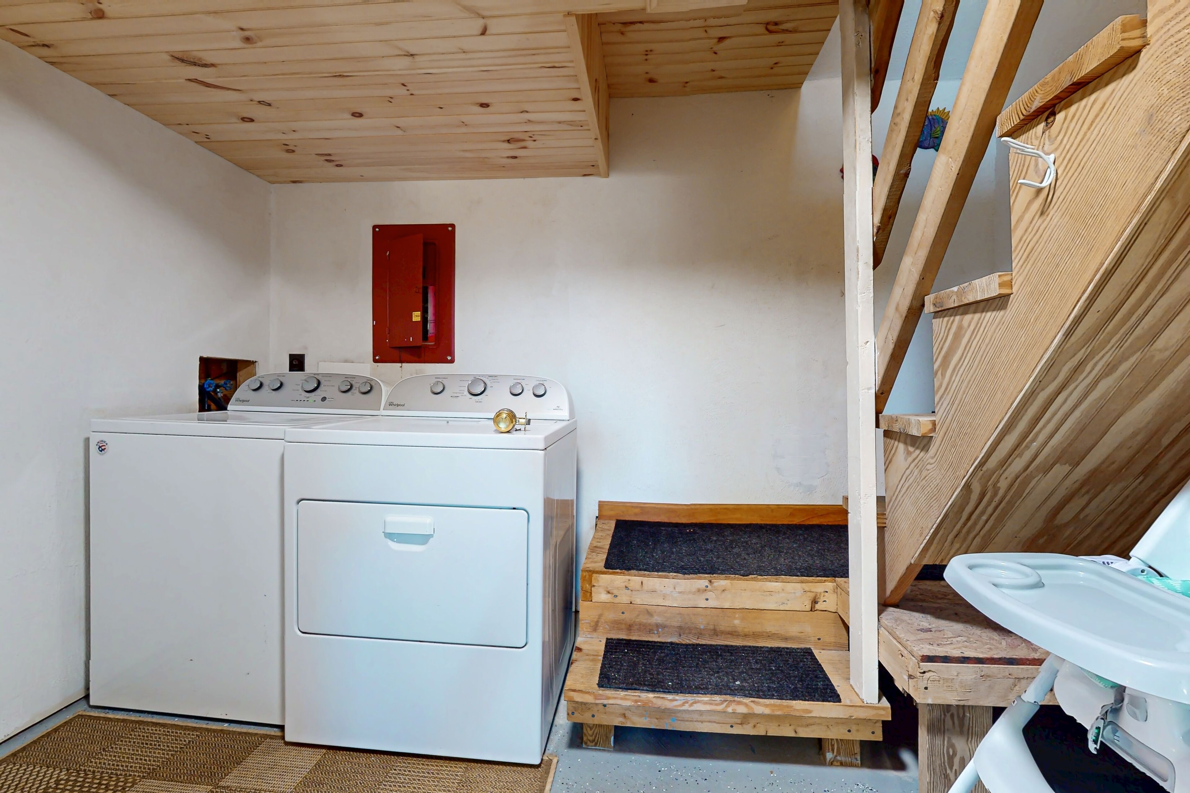 Une buanderie équipée d’un lave-linge, d’un meuble rouge et d’un tabouret en bois.