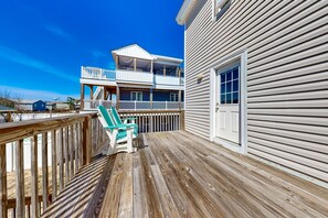 A wooden deck with a green chair, a balcony, and a white building with horizontal siding.
