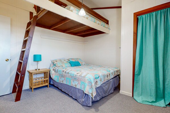 A bedroom with a bunk bed, a wooden ladder, a small bedside table with a lamp, and a green curtain.