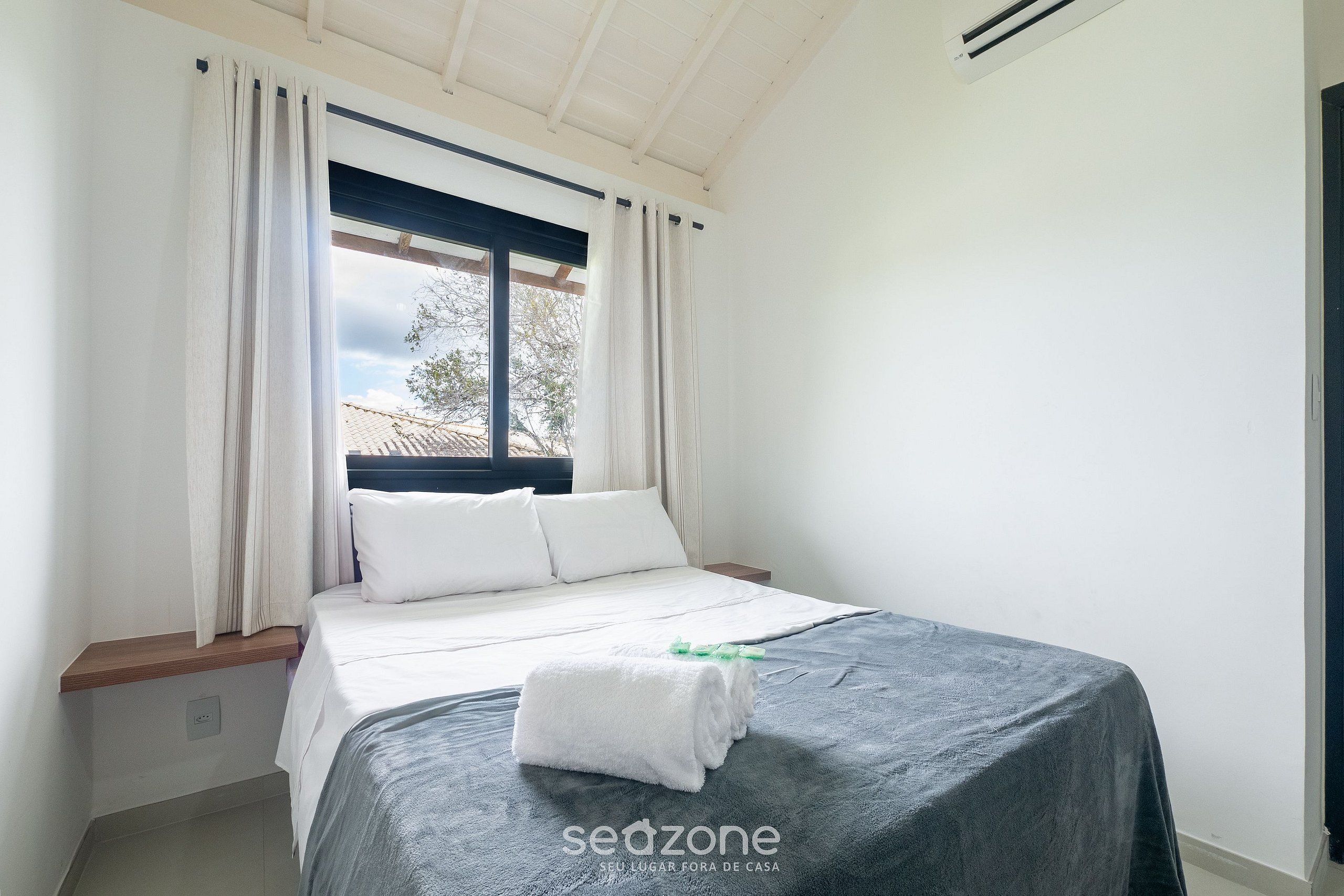 A bedroom with a bed, white curtains, a window, and a towel on the bed.
