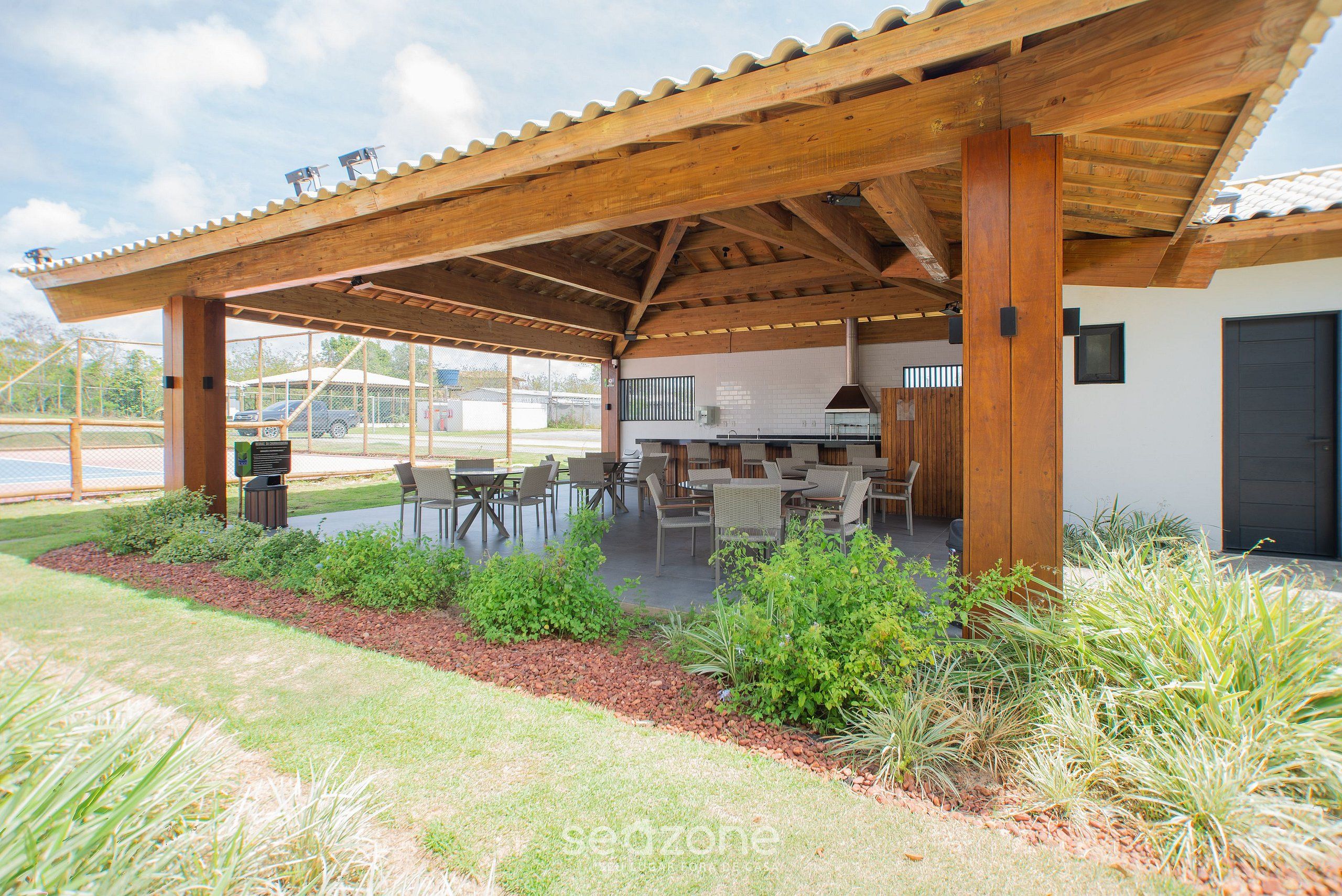 A covered outdoor seating area with tables and chairs, a barbecue grill, and a view of the surrounding landscape.
