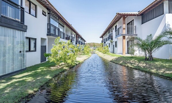 A canal running through a residential area with modern houses on either side. - Ap in a Cond. W/pool at Praia do Forte Cvaf0220 (Mata de São João)