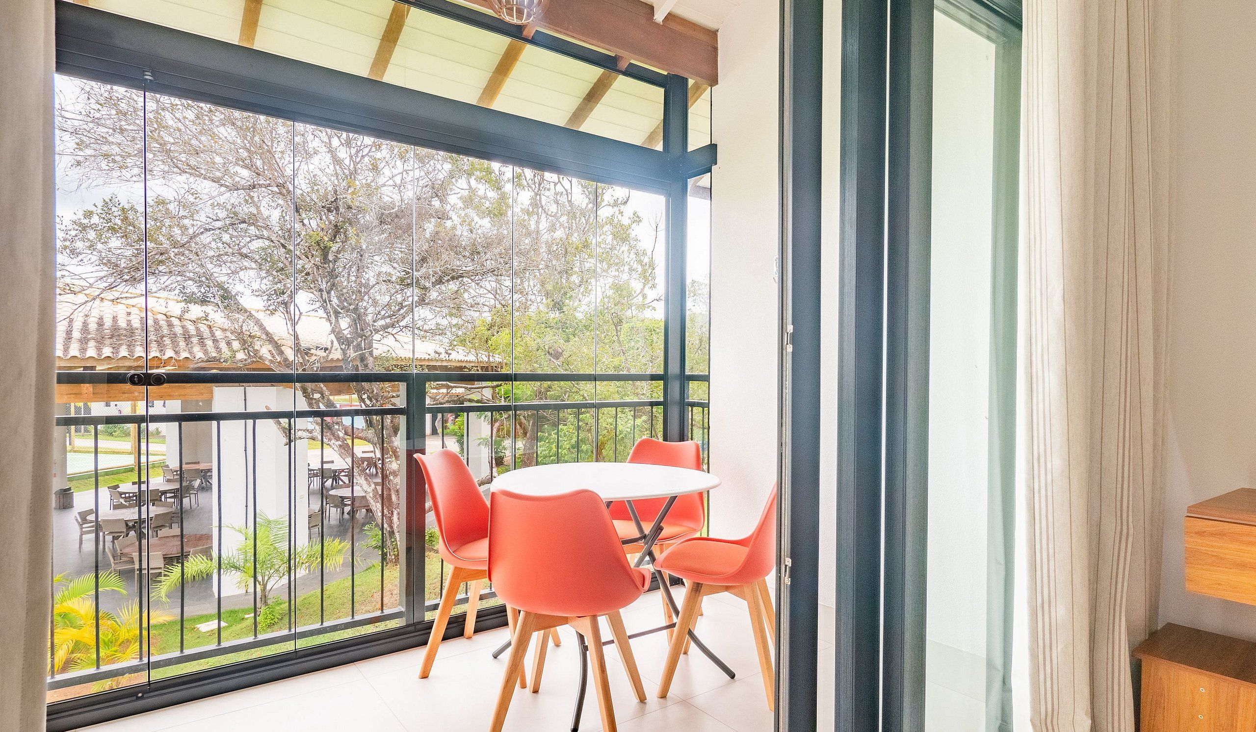 A balcony with a table and chairs, a view of a garden, and a building with a tiled roof.
