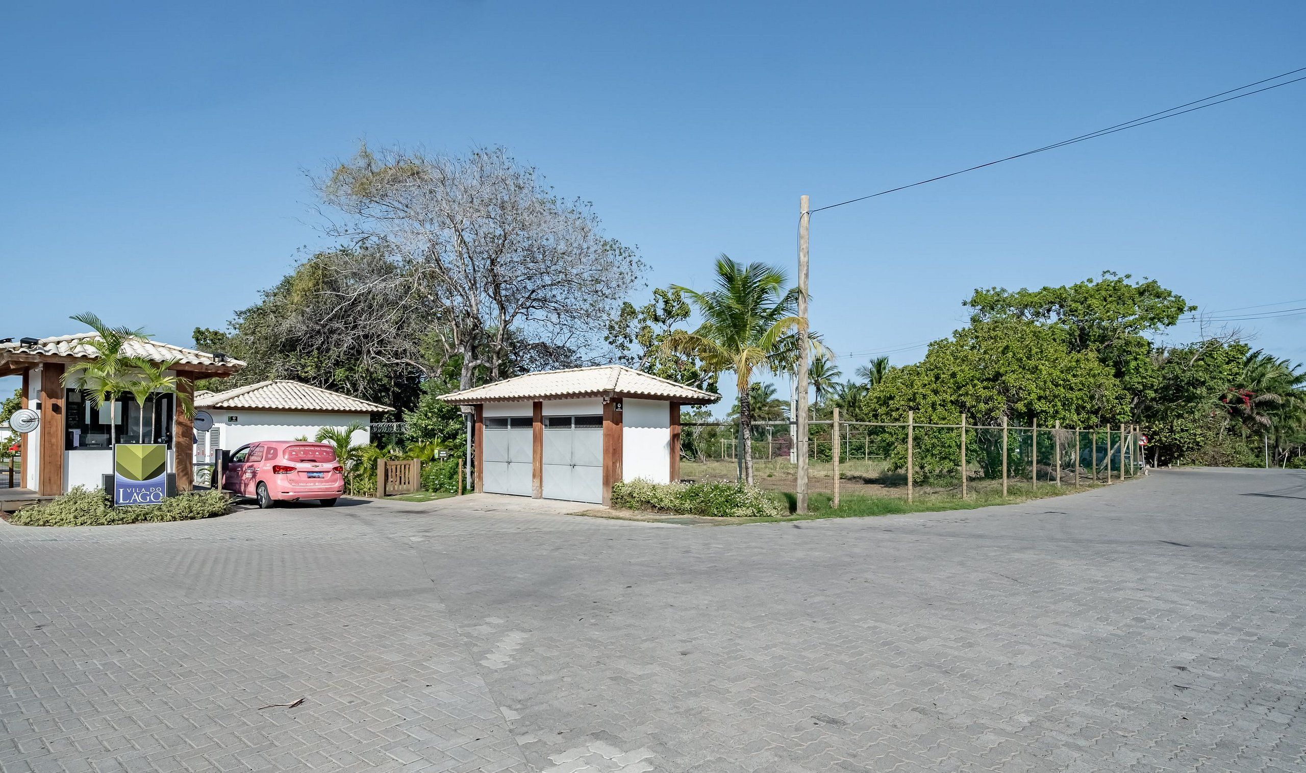 Una propiedad con dos edificios pequeños, un camino de acceso pavimentado y un área cercada con árboles.