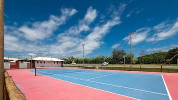 An outdoor tennis court with a net, surrounded by a fence and trees.