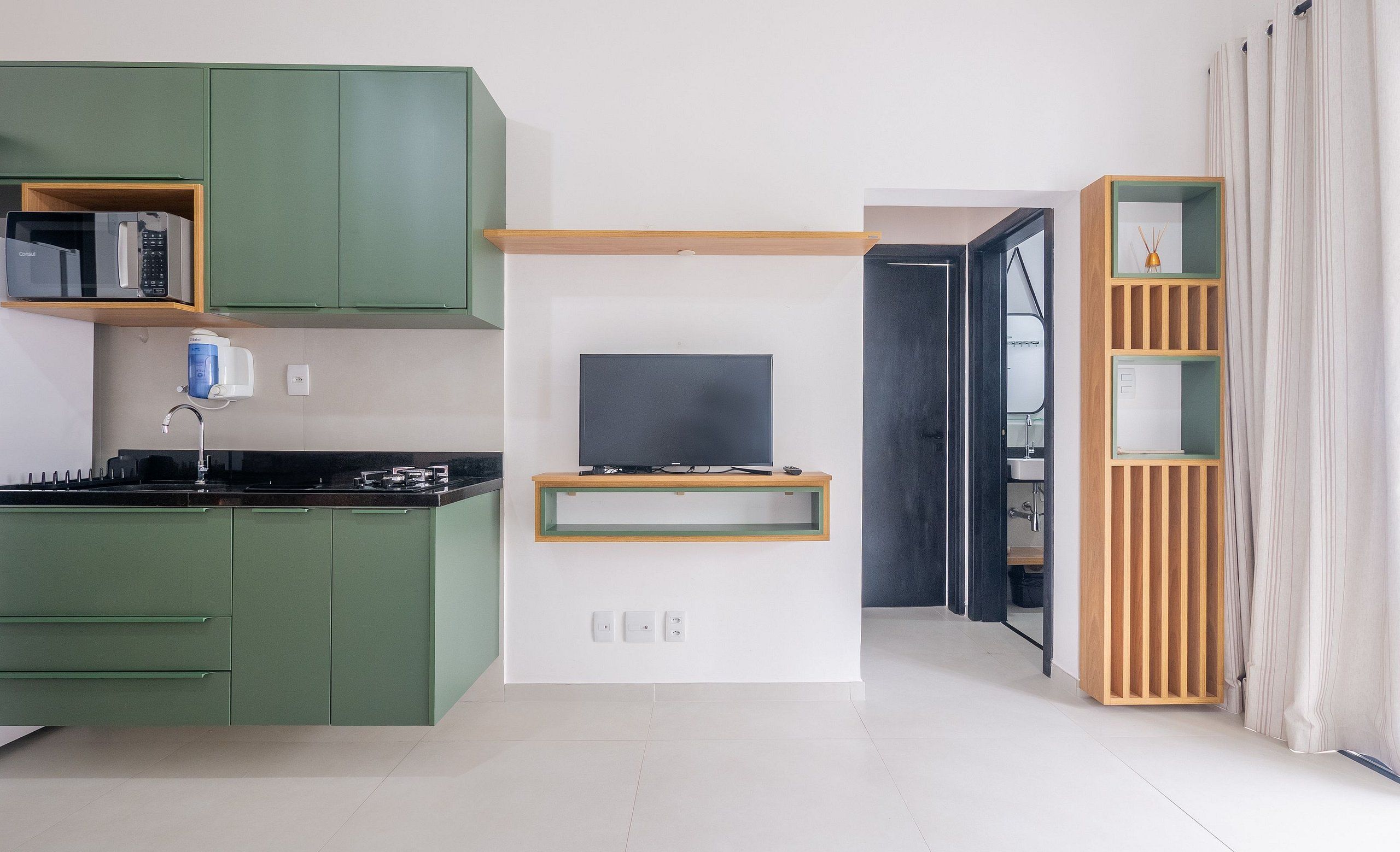 Una cocina moderna con armarios verdes, un microondas integrado y un televisor sobre un estante de madera.