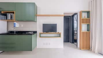 Una cocina moderna con armarios verdes, un microondas integrado y un televisor sobre un estante de madera.