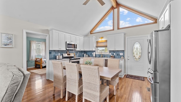A modern kitchen with white cabinets, a stainless steel refrigerator, and a dining area with wicker chairs.