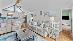 A spacious living area with a high ceiling, a large window, and a kitchen in the background.