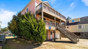 A two-story building with a balcony, a staircase, and a sign indicating a parking area. - CH50: The Sweet Pelican, 4BR home with Shared Pool- pet friendly (Kill Devil Hills)