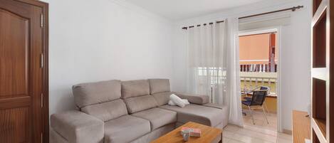 A living room with a sofa, a wooden coffee table, a door, and a view of an outdoor balcony.