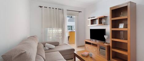 A modern living room with a sofa, coffee table, TV stand, and wooden shelving unit.