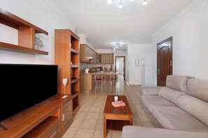 Una sala de estar con televisor, estanterías de madera, un sofá y una cocina al fondo.