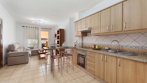 Cuina moderna amb armaris de fusta, una illa central amb tamborets, forn integrat i una finestra gran.