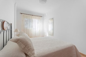 A bedroom with a bed, curtains, a lamp, and a window. - Apartment at Playa San Juan (Playa San Juan)