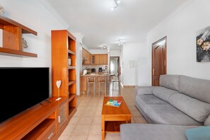 Un soggiorno con televisore, mensole in legno, un divano grigio e, sullo sfondo, una zona pranzo.