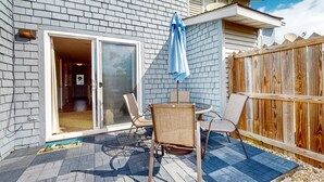Une terrasse avec une table et des chaises, une clôture en bois et une porte-fenêtre coulissante donnant sur un espace intérieur.