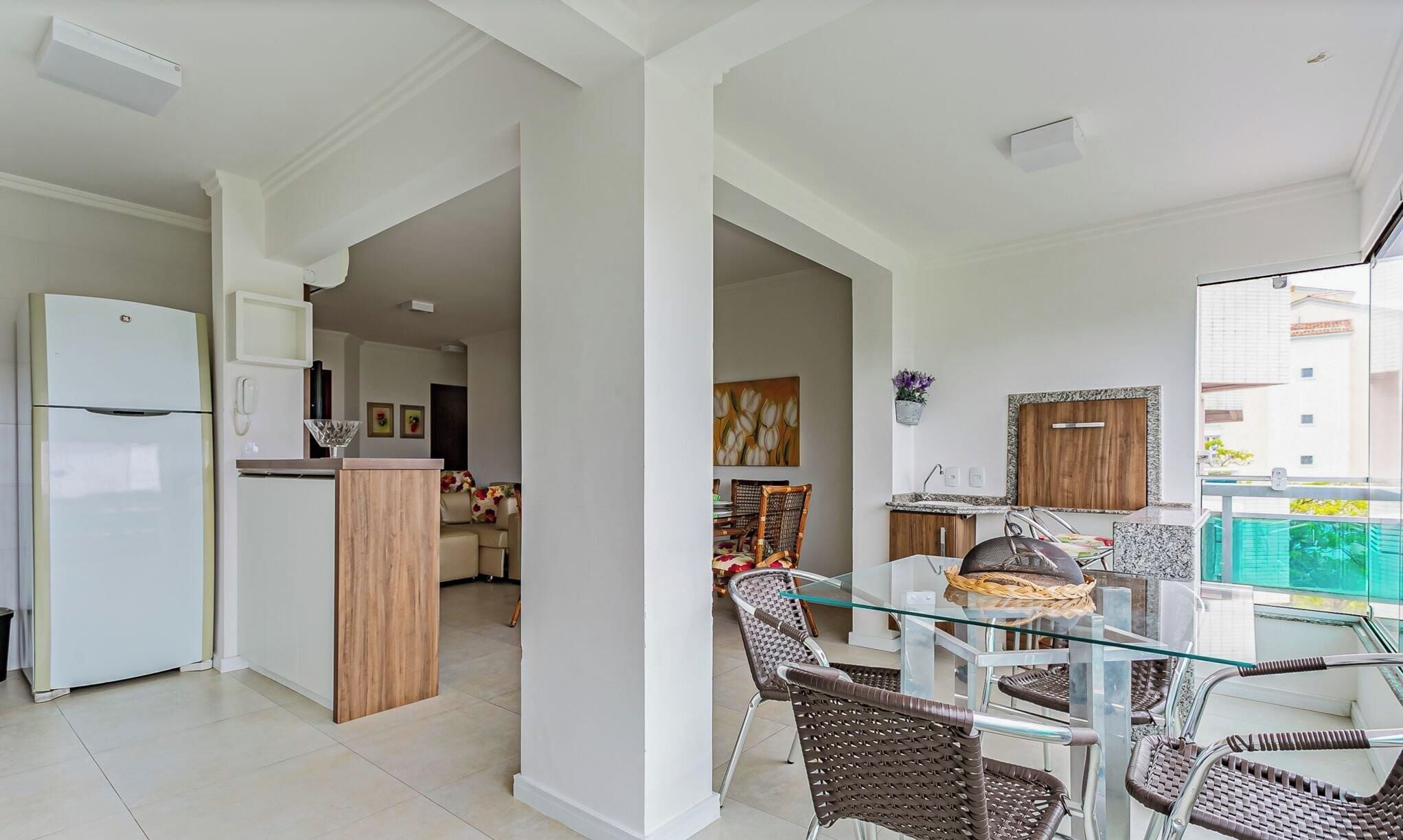 A modern kitchen with a refrigerator, a dining area with wicker chairs, and a glass-top table.