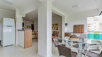 A modern kitchen with a refrigerator, a dining area with wicker chairs, and a glass-top table.