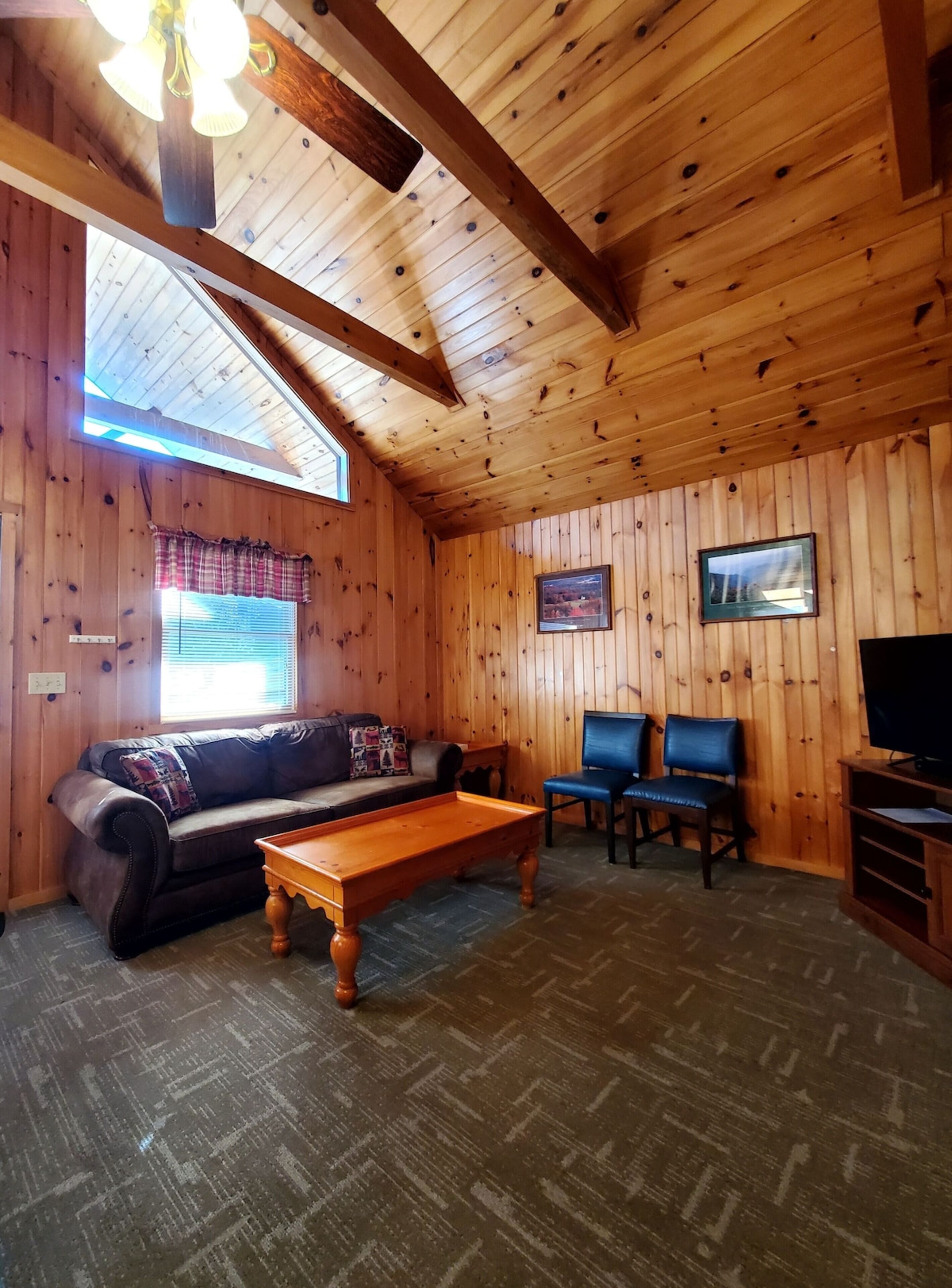 Una habitación con paneles de madera, un sofá, dos sillones, una mesa de centro, un televisor y un ventilador de techo.