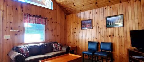 Una habitación con paneles de madera, un sofá, dos sillones, una mesa de centro, un televisor y un ventilador de techo.