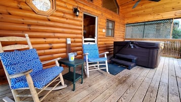 A wooden cabin with a porch featuring rocking chairs, a table, and a hot tub.