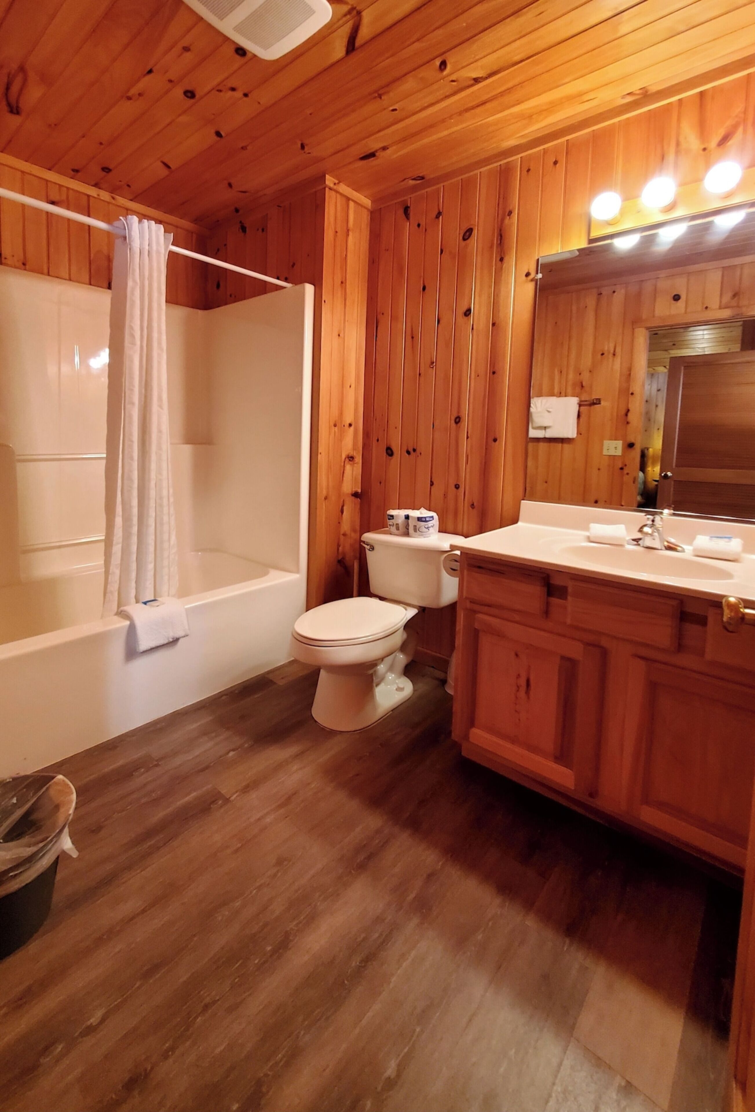 A wooden-paneled bathroom with a bathtub, toilet, and vanity.