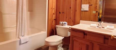 A wooden-paneled bathroom with a bathtub, toilet, and vanity.