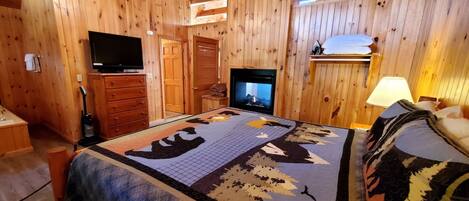 A wooden cabin room with a bed, a television, a fireplace, and a ceiling fan.