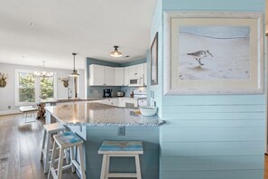 A kitchen with white cabinets, a granite countertop, and a framed seashore painting.