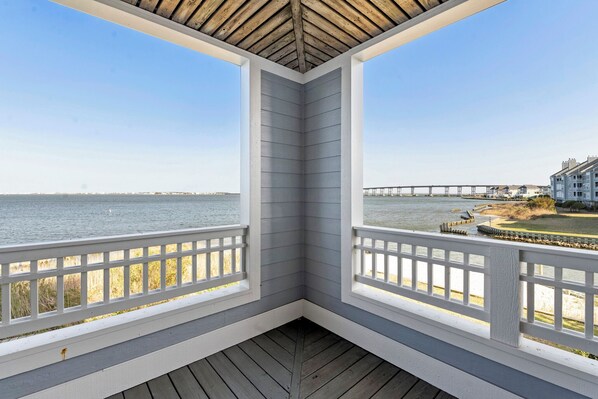 A corner view of a wooden deck with a railing, overlooking a body of water and a pier.