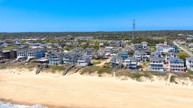 A coastal residential area with beachfront houses, a clear sky, and a distant communication tower. - 5BR Oceanview | Private Pool | Hot Tub | Balcony (Nags Head)