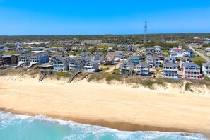 A coastal residential area with beachfront houses, a clear sky, and a distant communication tower.