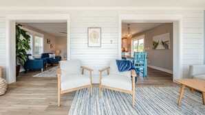 A spacious living area with a large plant, a blue sofa, and a dining area with a wooden table and chairs.