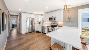 A modern kitchen with white cabinets, stainless steel appliances, and a wooden floor.