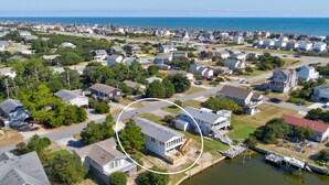 An aerial view of a coastal residential area with houses, a dock, and a body of water.