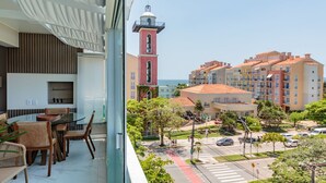 Un balcón con zona de comedor, vista a un pueblo con edificios y una torre, y cielo despejado.