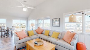 A modern living room with a large gray sectional sofa, a wooden coffee table, and a dining area with a table and chairs.