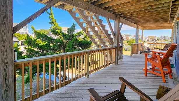 A wooden deck with a railing, outdoor seating, and a view of houses and trees.