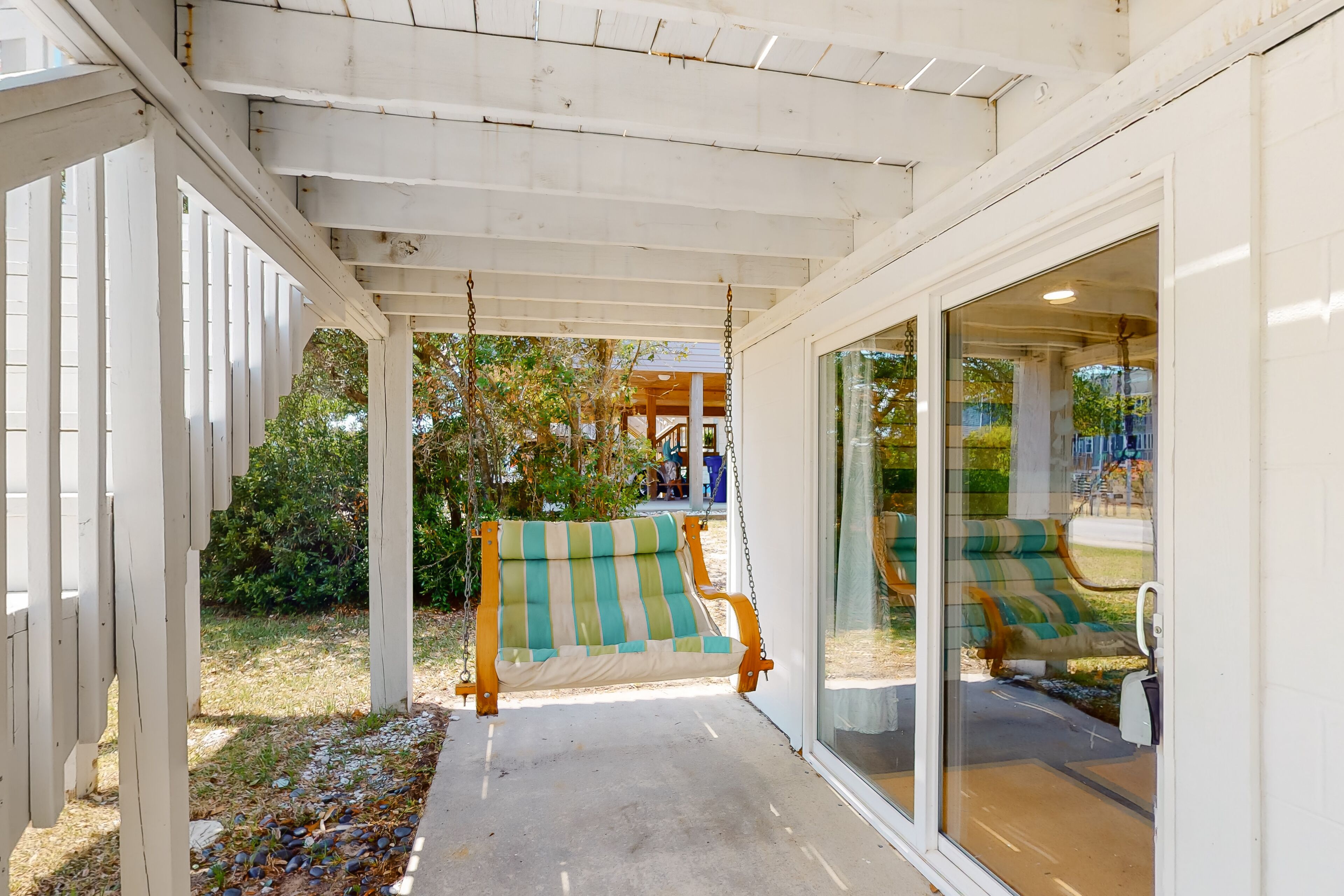 A covered porch with a wooden swing and a glass door leading to a patio area.
