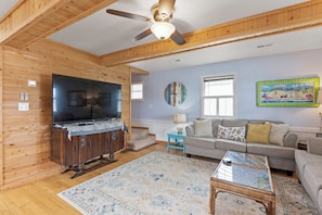 A wooden interior with a ceiling fan, a flat-screen TV, a sofa, a coffee table, and a patterned rug. - 2BR Soundview | Balcony | W/D (Nags Head)