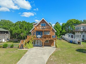 A two-story wooden house with a front porch, a basketball hoop, and a fenced yard.