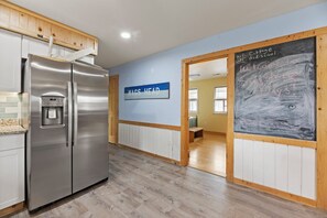 A kitchen with a stainless steel refrigerator, a water dispenser, and a sign indicating a 'MAGS HEAD' area.