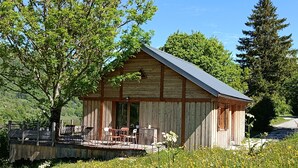 A rustic wooden cabin with a porch and outdoor seating, surrounded by a field of wildflowers and trees.