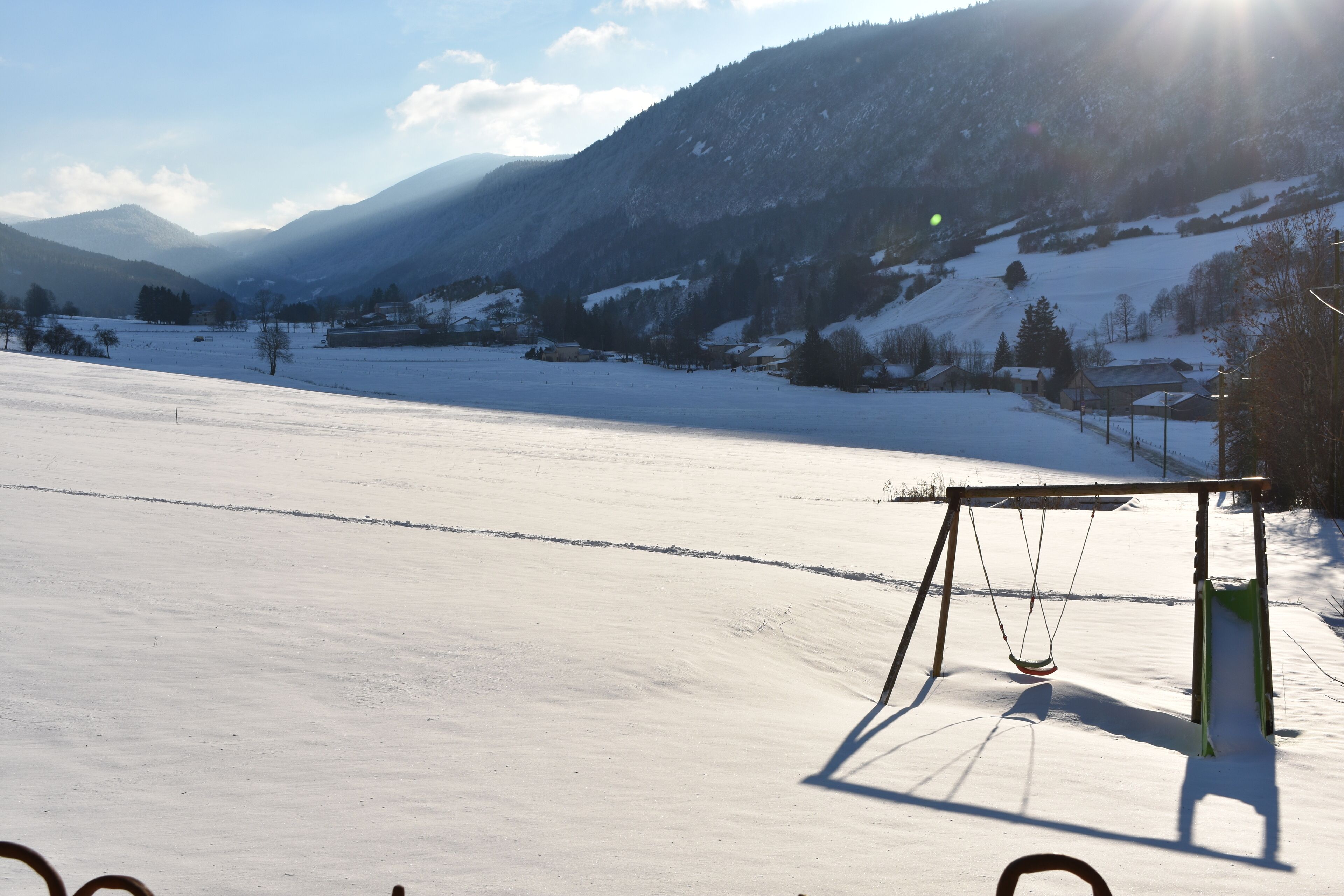 A snow-covered landscape with a swing set in the foreground.
